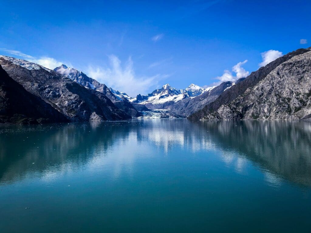 Dramatic snow capped rocky mountains reflect off the waters along Alaska's coast line.